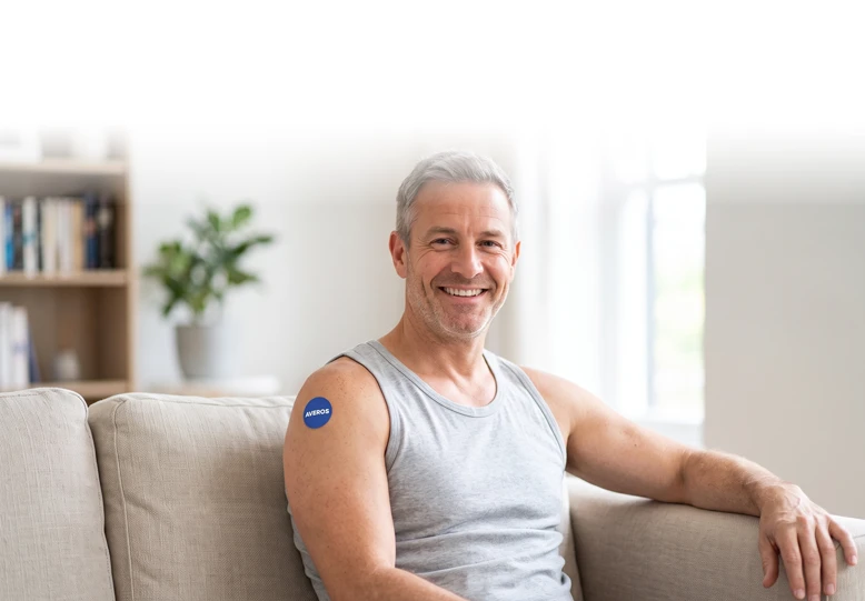 Lächelnder Mann um die fünfzig auf dem Sofa mit einem runden blauen Averos Pflaster
